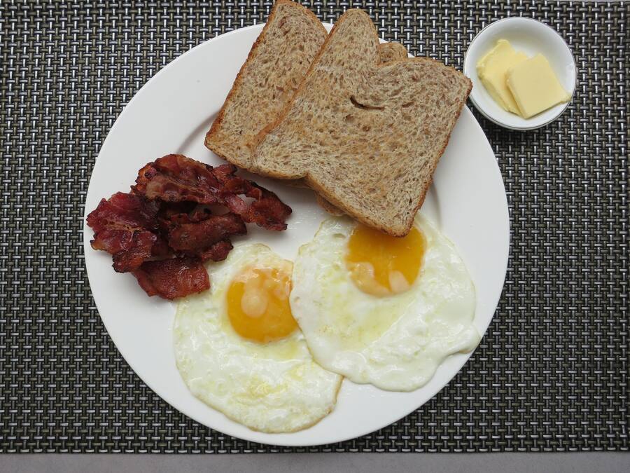 Un plato con tostadas, tocino y huevos fritos sobre un posavasos tejido.