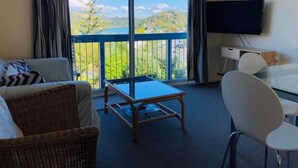 Une chambre d’hôtel avec un balcon, un canapé, un fauteuil, une petite table et un téléviseur.