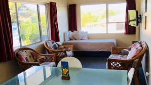 Une pièce avec une table en verre, deux chaises blanches, un lit avec un matelas bleu et une fenêtre avec des rideaux rouges.