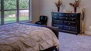 Une chambre avec un grand lit, un ventilateur de plafond, une commode et une fenêtre donnant sur un paysage verdoyant.