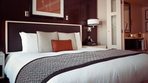 Une chambre d’hôtel avec un grand lit, une tête de lit, une table de chevet avec une lampe et une œuvre d’art encadrée accrochée au mur.