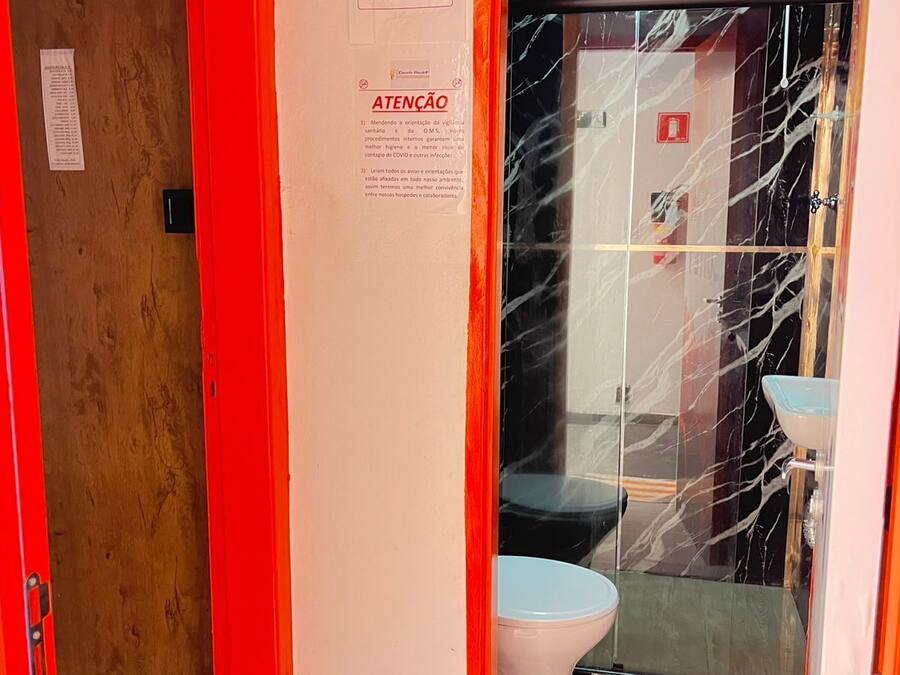 Casa de banho com lavatório de mármore, sanita e porta com moldura vermelha.