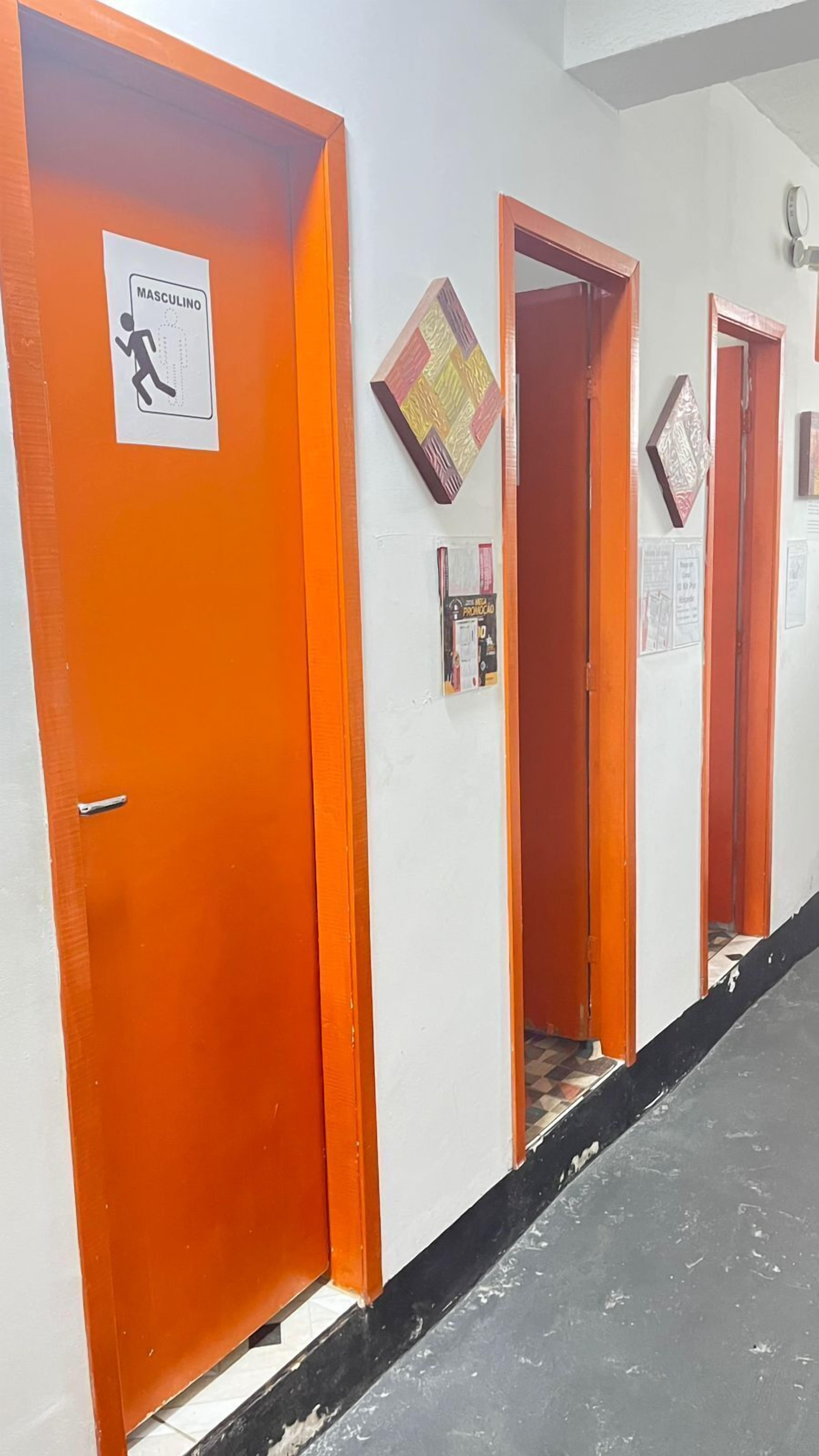 Een gang met oranje deuren, waarvan enkele bordjes hebben met aanduiding van geslachtsgebonden toiletten.