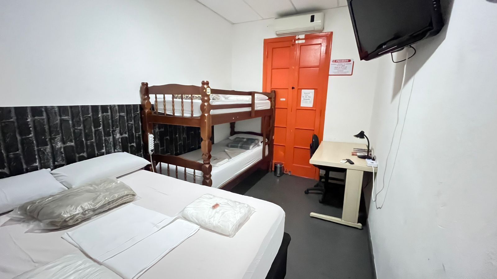 A room with a bunk bed, a desk, a chair, and a television mounted on the wall.