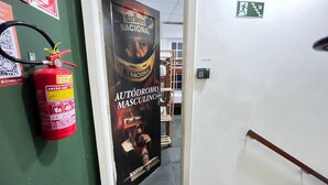 Um corredor com um extintor de incêndio, um cartaz na parede e uma porta com sinal de saída de emergência.