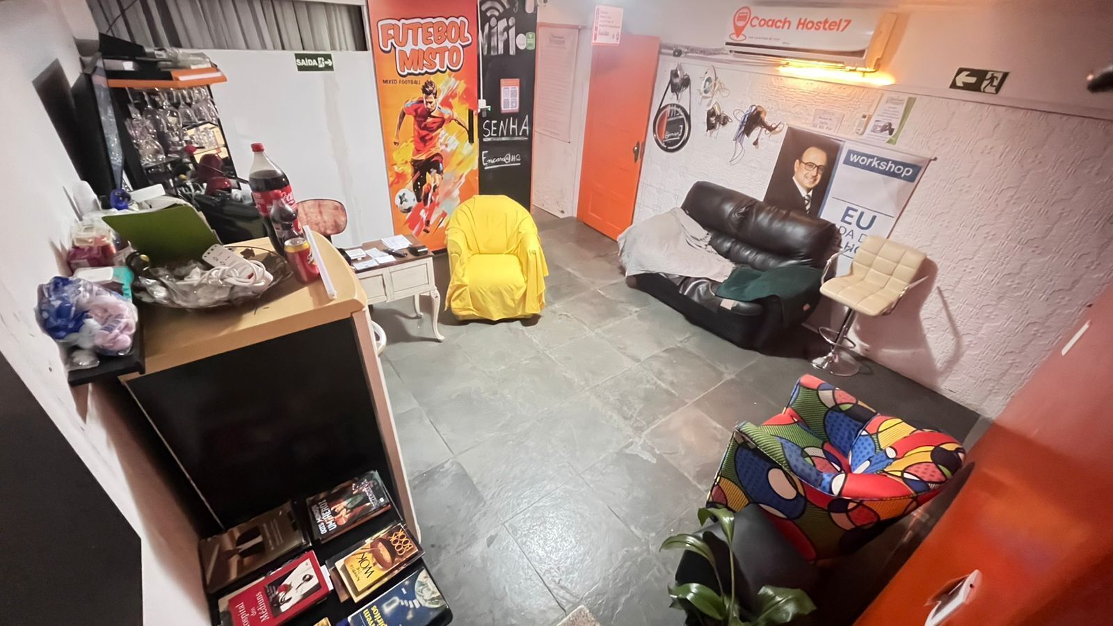 A room with a TV, a couch, a chair, a table with items, and a poster on the wall.