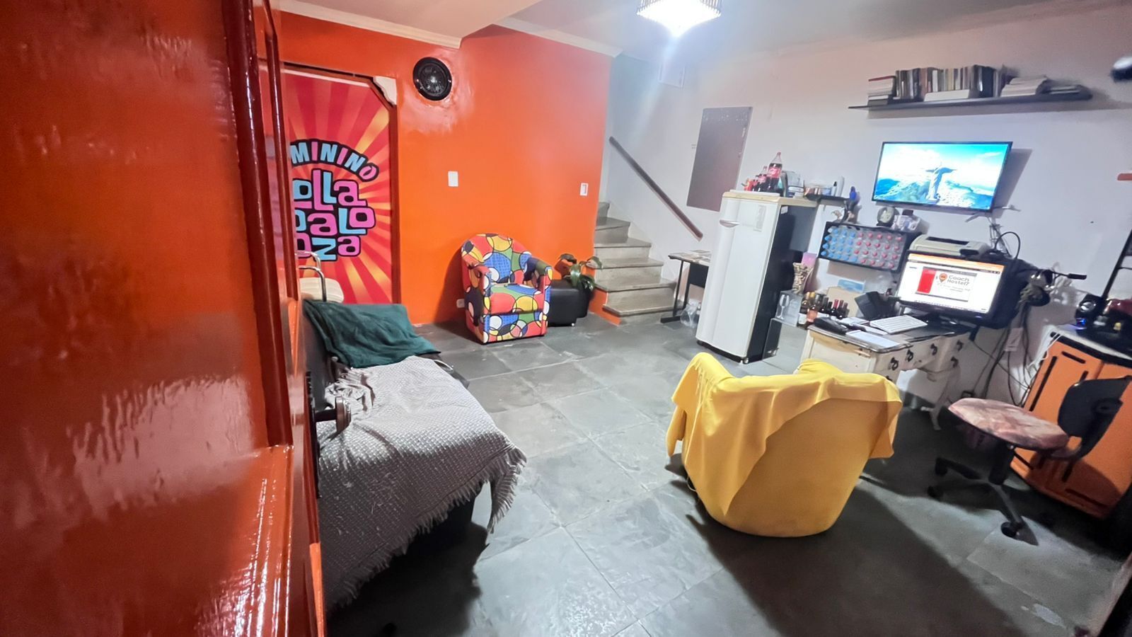 Una habitación compacta con una cama, una silla amarilla, un escritorio con una computadora y un televisor.