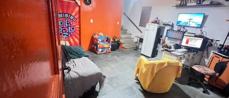 Una habitación compacta con una cama, una silla amarilla, un escritorio con una computadora y un televisor.