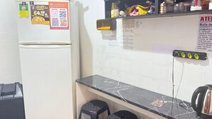 Uma pequena cozinha compacta com geladeira, bancada preta e prateleira na parede com diversos objetos.