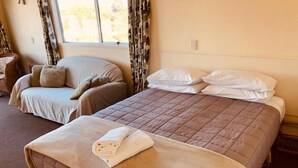 Une chambre d’hôtel avec deux lits, un canapé et une fenêtre avec des rideaux.