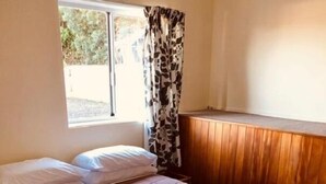 Un lit bien fait, avec une tête de lit matelassée, une fenêtre donnant sur un paysage verdoyant et un panneau de bois le long du mur.