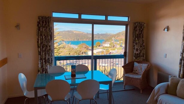 Une chambre avec balcon, une table à manger avec des chaises, un canapé et une vue sur un lac et des collines.
