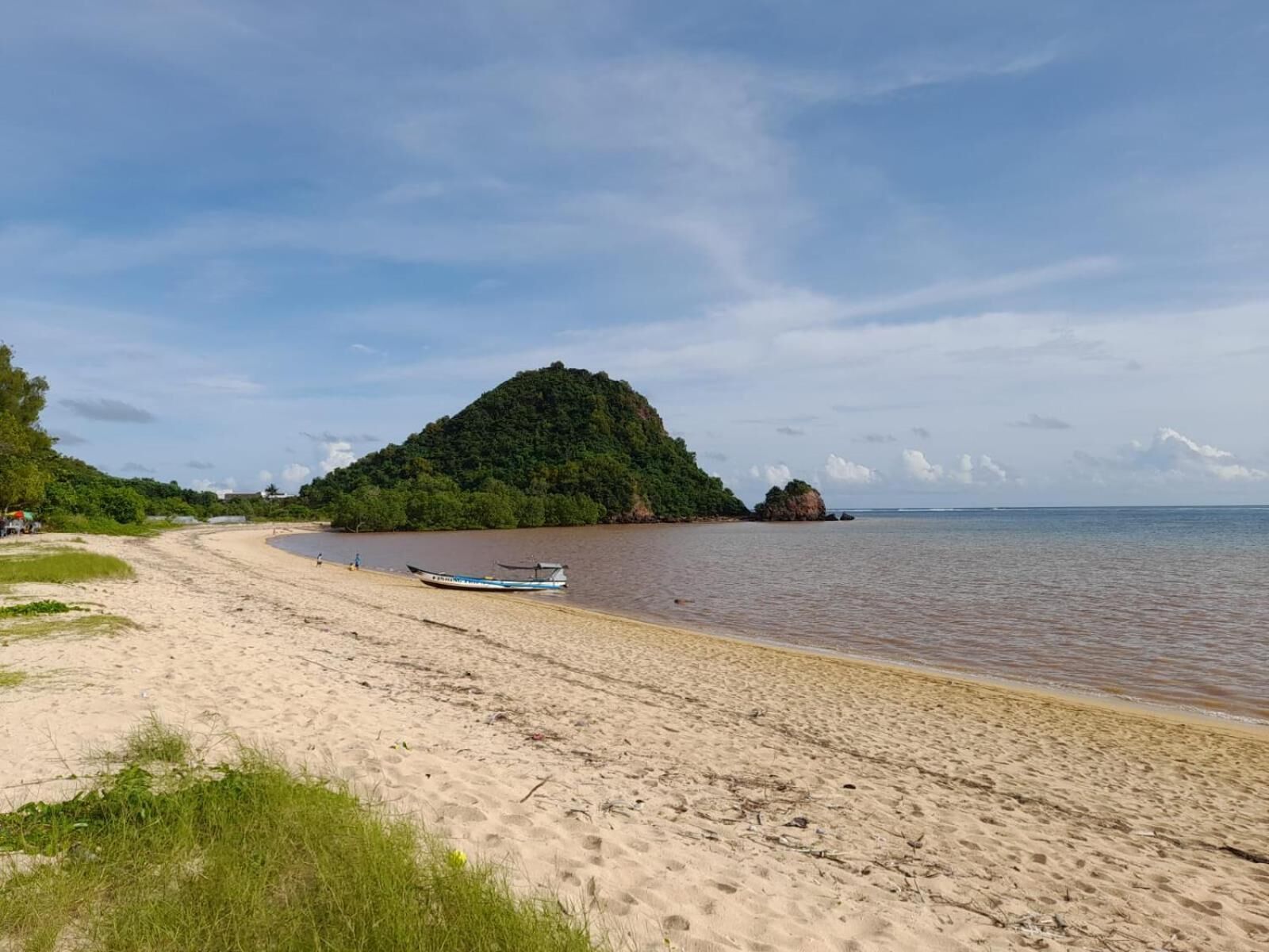 A sandy beach with a boat, a small island, and a clear sky.