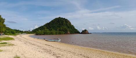 A sandy beach with a boat, a small island, and a clear sky.