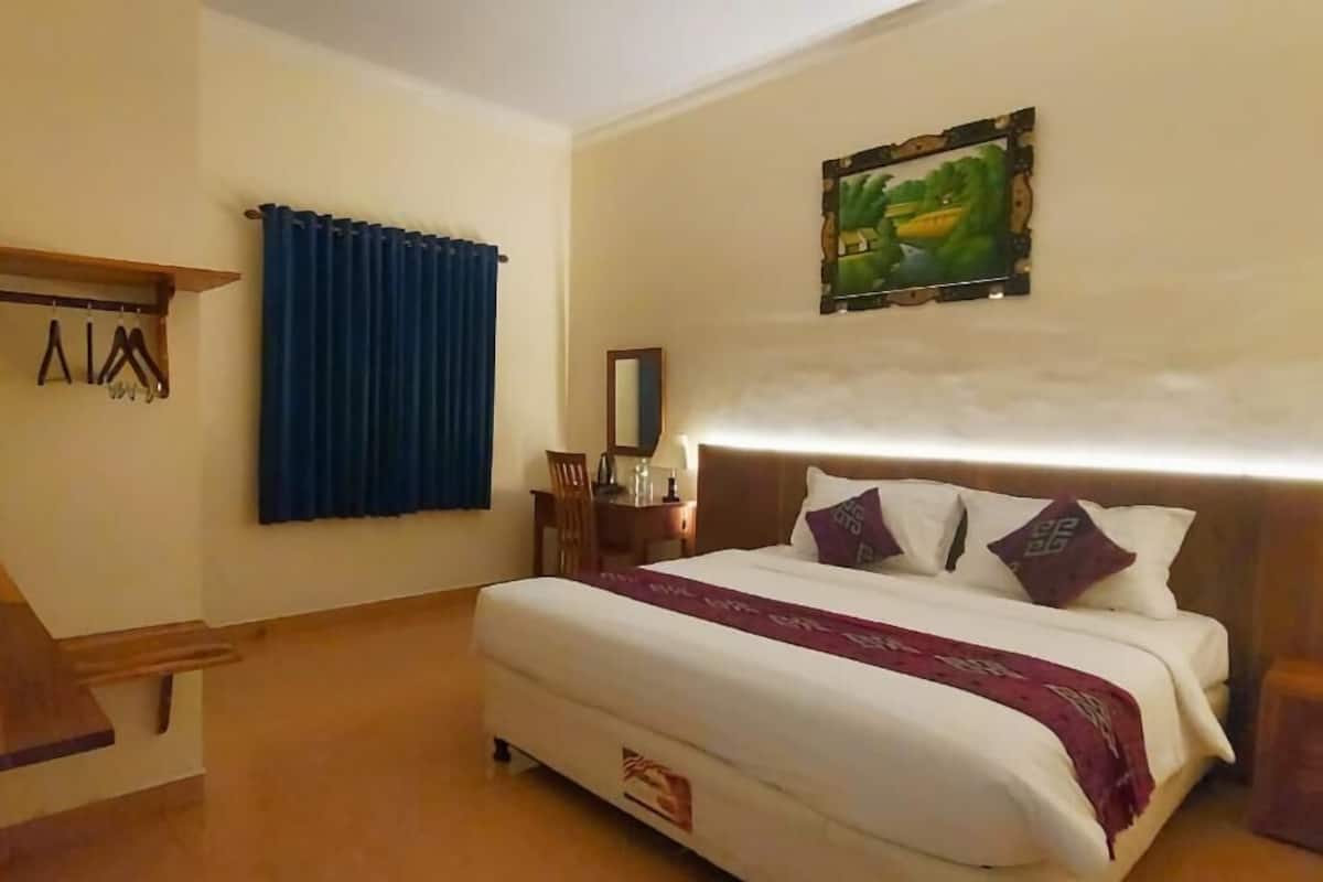 A hotel room with a bed, a desk, a chair, a TV, and a painting on the wall.
