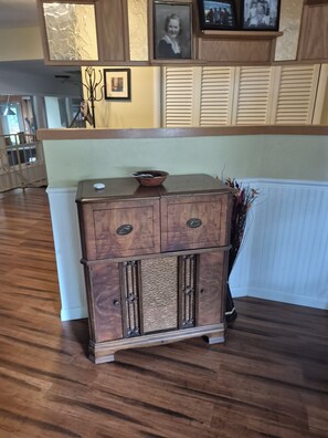 A wooden cabinet with two drawers and a bowl on top, placed against a wall with a window and blinds.