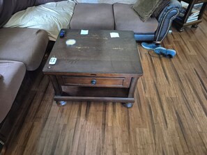 Una mesita auxiliar de madera con un cajón, un control remoto y un pequeño recipiente encima.