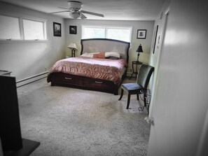 Een slaapkamer met een bed, een stoel, een plafondventilator en een raam.