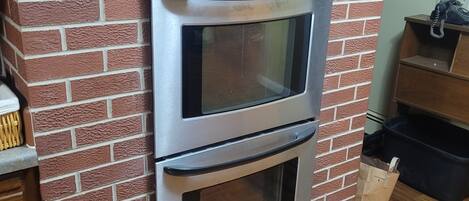 A kitchen with a brick wall, a double oven, and a wooden countertop.