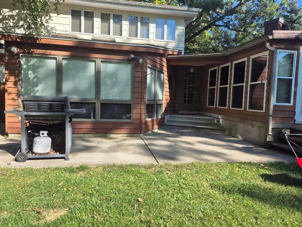 A two-story house with a front porch, a grill, and a propane tank.