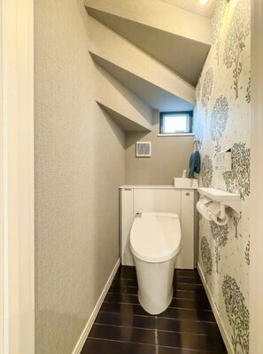 Bathroom features a modern toilet, dark tile floor, and floral wallpaper.