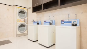 Une laverie équipée de trois machines à laver à pièces et d’une grande machine à laver fixée au mur.