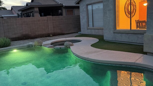 A modern house with a swimming pool, a brick wall, and a large window with blinds. - Oasis at Johnson Ranch (Queen Creek)