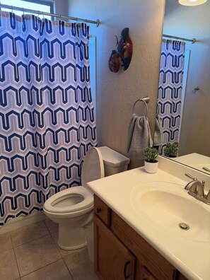 Ein Badezimmer mit einem waschmusternden Duschvorhang, einer Toilette, einem Waschbecken mit Spiegel und einem Handtuchhalter.