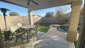 A covered patio with a table and chairs, a ceiling fan, and a swimming pool. - Oasis at Johnson Ranch (Queen Creek)