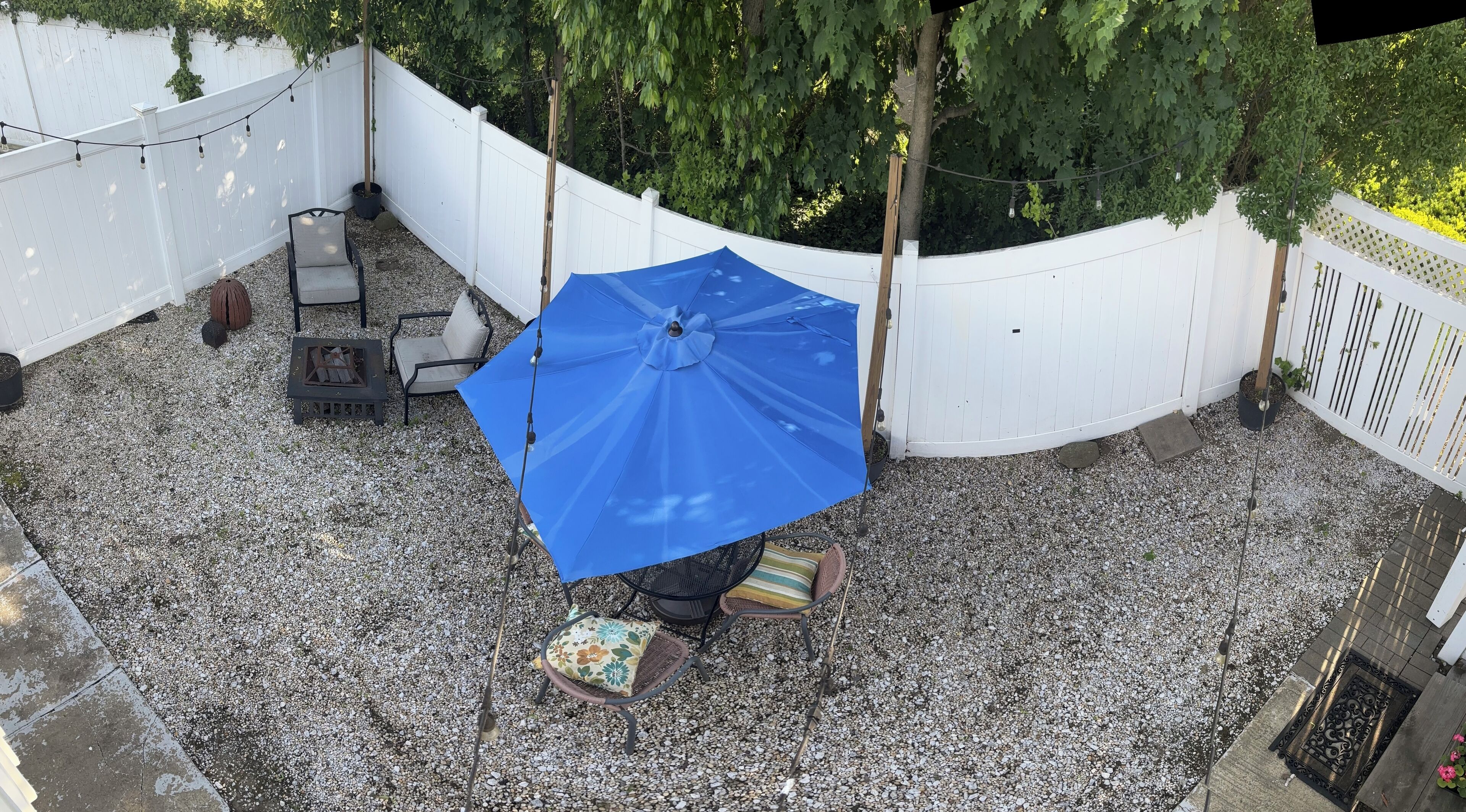 A patio area with a blue umbrella, outdoor furniture, and a white fence.