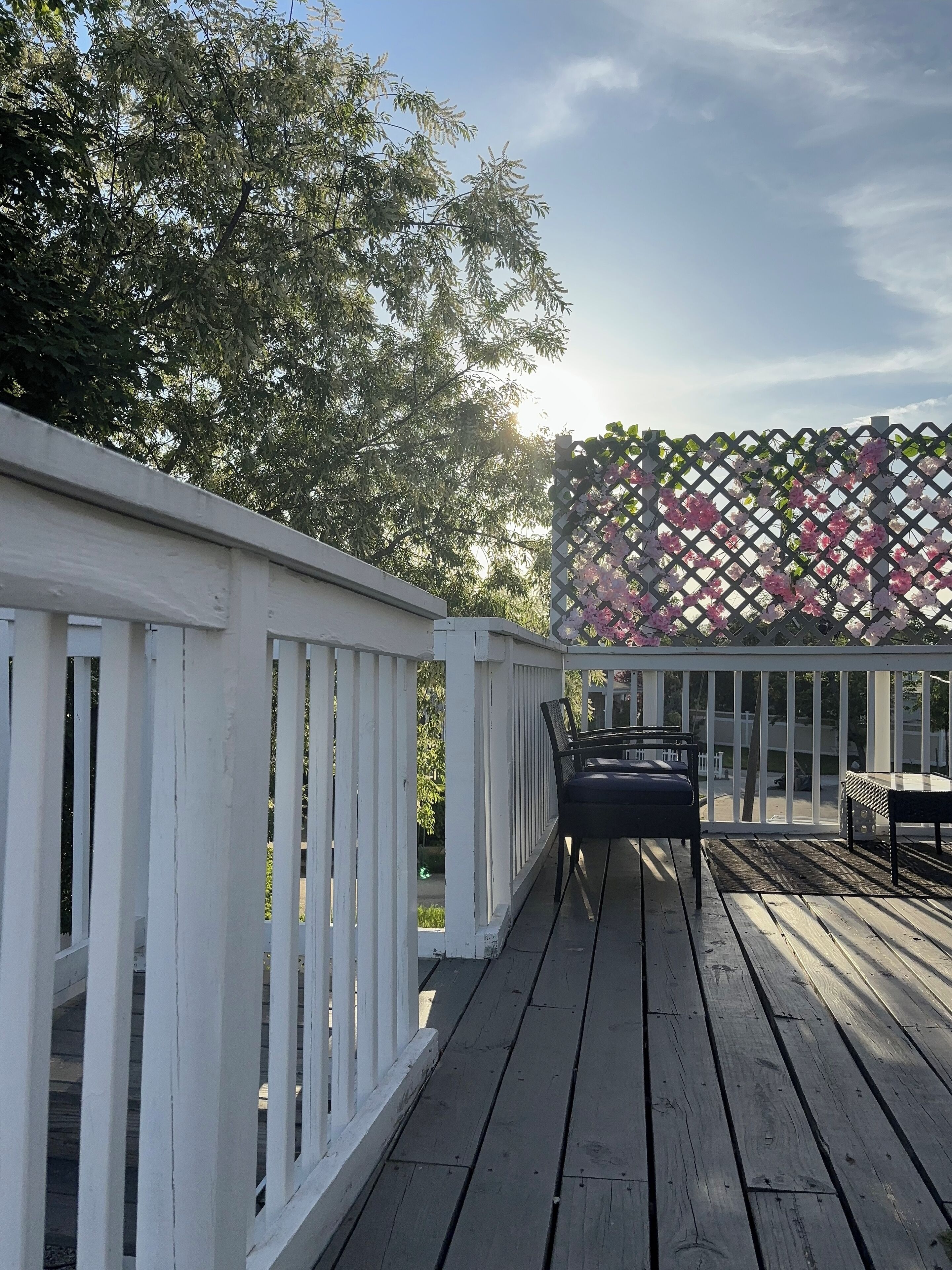 Un pontile in legno con ringhiere bianche e una struttura a griglia decorata con fiori rosa.