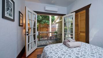 Um quarto com cama, janela e porta aberta para um pátio.