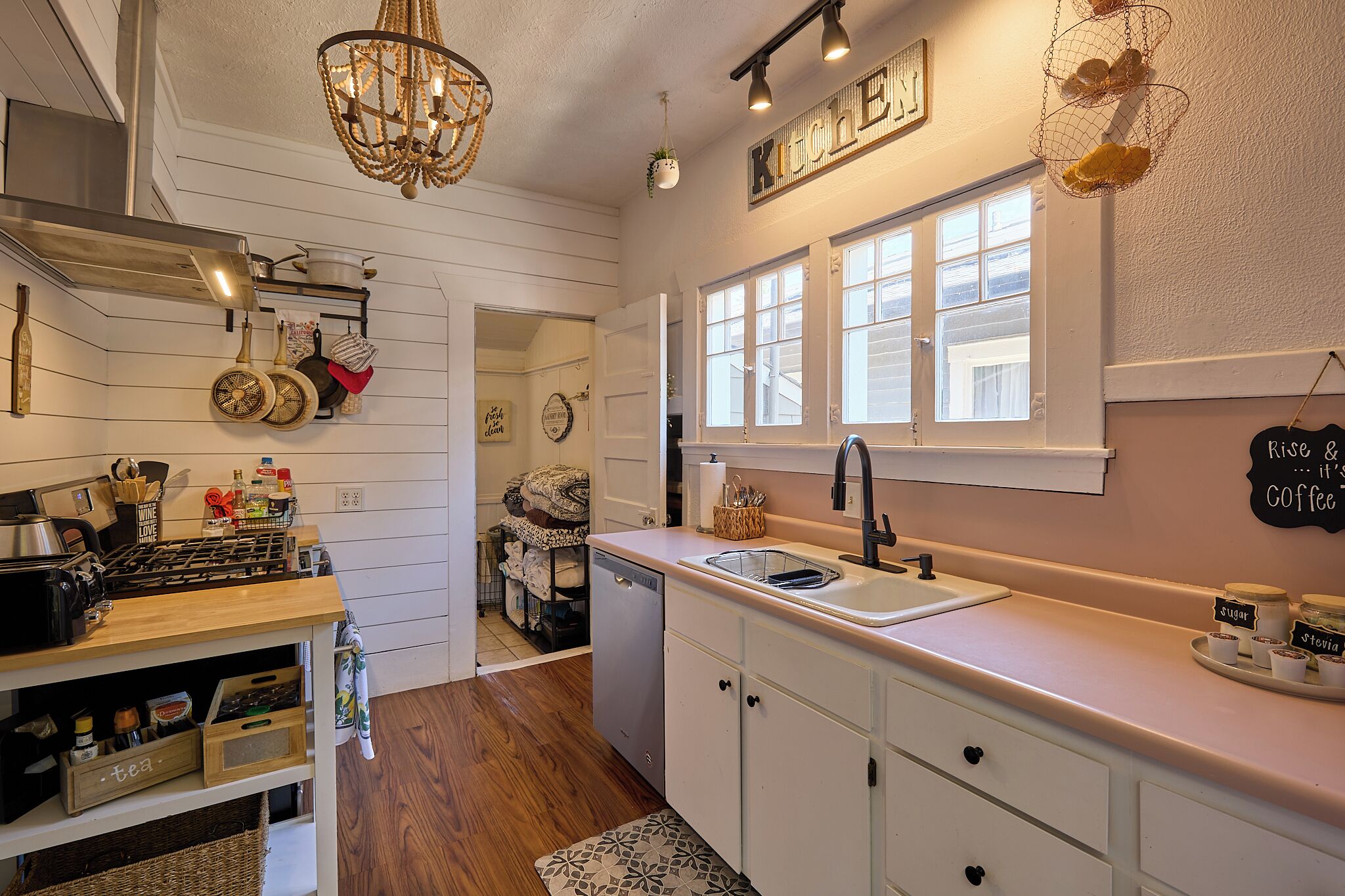 A kitchen with white cabinets, a wooden countertop, a sink, and a chandelier. There are jars labeled "sugar" and "strawberry" on the counter.