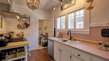 A kitchen with white cabinets, a wooden countertop, a sink, and a chandelier. There are jars labeled "sugar" and "strawberry" on the counter.