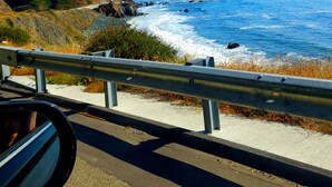 A coastal road with a guardrail, a clear blue sky, and the ocean in the distance.