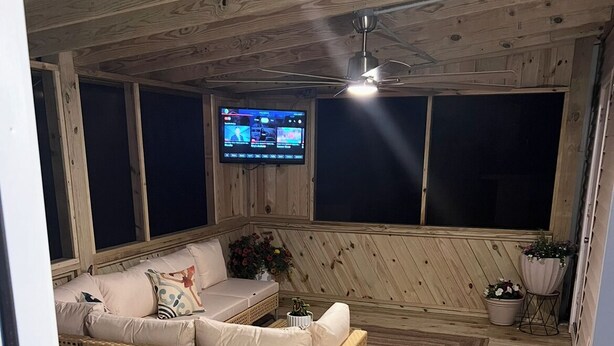 Una habitación acogedora con un sofá de mimbre, un televisor montado en la pared y un ventilador de techo.