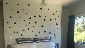 Un letto con biancheria bianca, una parete con motivo geometrico e una lampada a sospensione.