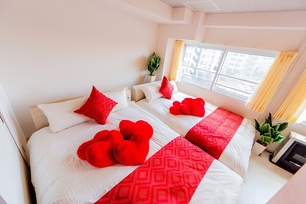 Habitación de hotel con dos camas, almohadas con forma de corazón rojo y una colcha de diseño geométrico.