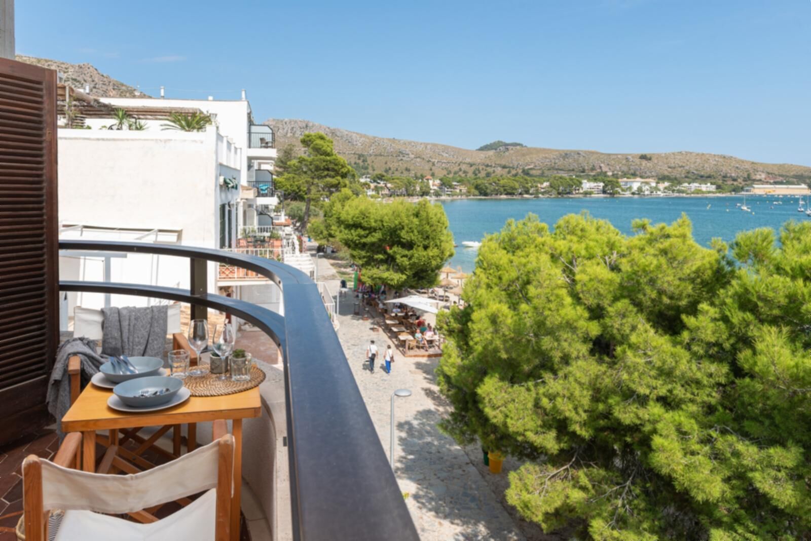 A balcony with a table set for dining, overlooking a beach with trees and a view of the sea.