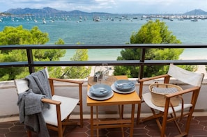A balcony with two wooden chairs, a small table, and a view of the sea with boats.