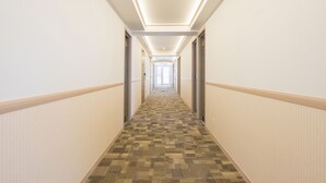 A hotel hallway with carpeted flooring, white walls, and doors on both sides. - Toyoko Inn Omori (Tokyo)