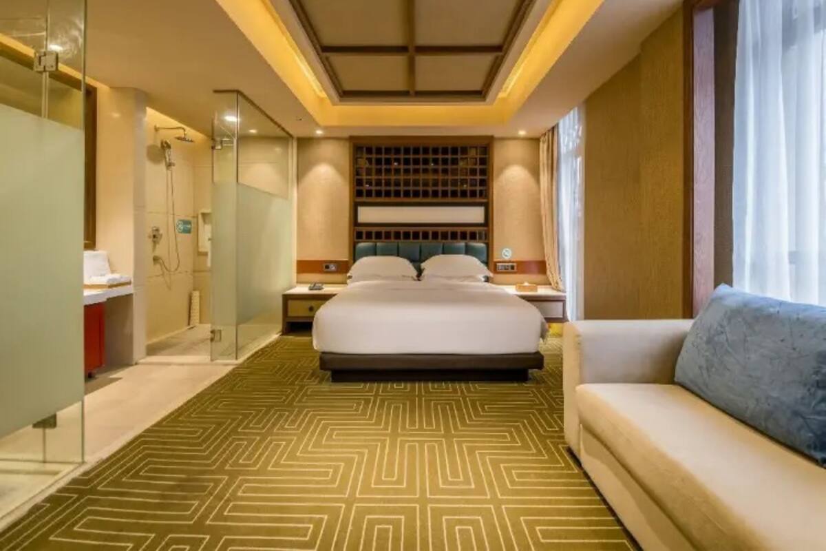 A hotel room with a large bed, a sofa, a walk-in closet, and a shower area.