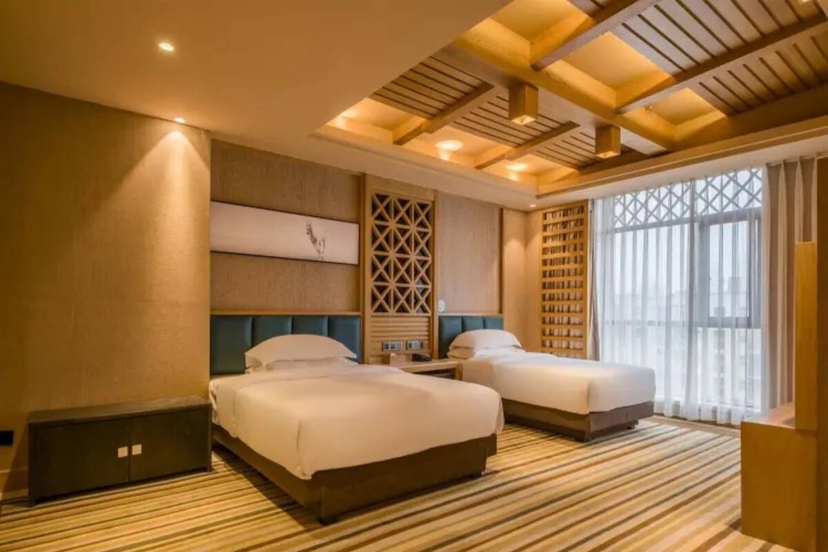 A hotel room with two beds, a large window, and a wooden ceiling design.