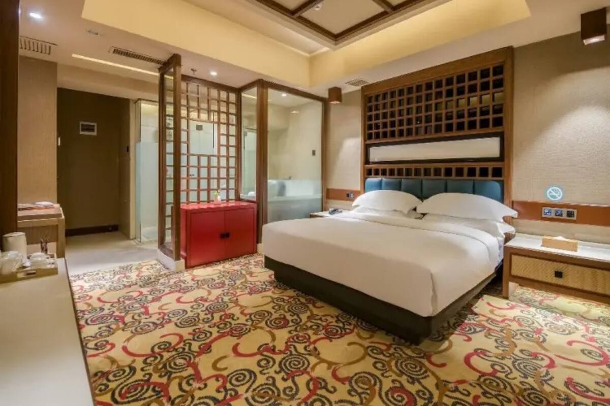 A hotel room with a bed, a nightstand, a red dresser, and a patterned carpet.