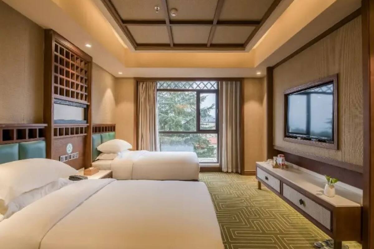 A hotel room with two beds, a large window, a TV, and a minibar.