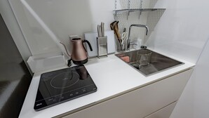 Ett kök med en inbyggd induktionshäll, en vattenkokare och ett handfat.