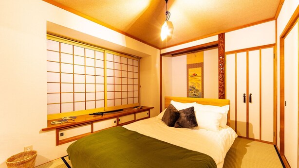 Una camera da letto tradizionale giapponese con pavimento in tatami, un futon, porte scorrevoli e una finestra con schermo shoji.