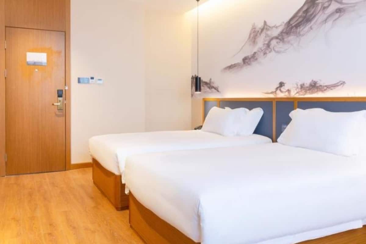 A hotel room with two beds, wooden flooring, a large wall-mounted artwork, and a wooden door.