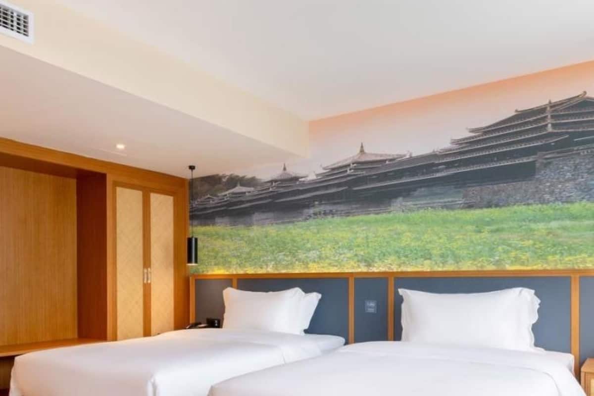 A hotel room with two beds, wooden flooring, a large mural of traditional architecture, and a wooden wardrobe.