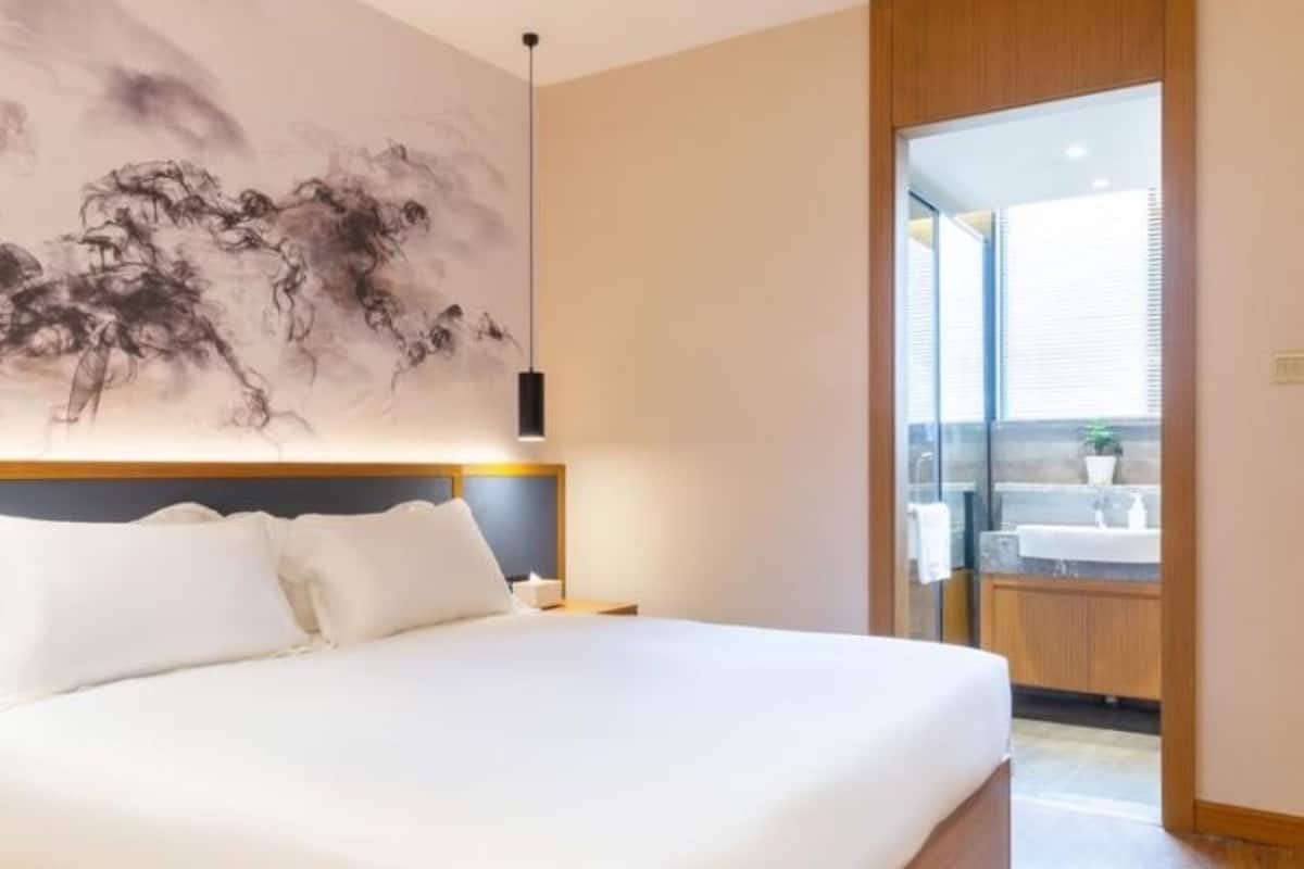 A modern bedroom with a large bed, a wall-mounted artwork, and a view of the bathroom through an open door.